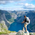 man standing on rock looking towards lake