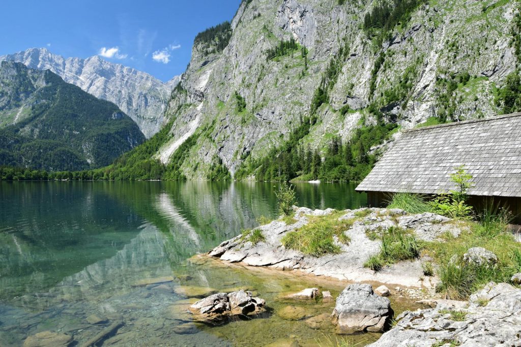 Stunning mountain lake view with reflections and a wooden cabin by the shore.